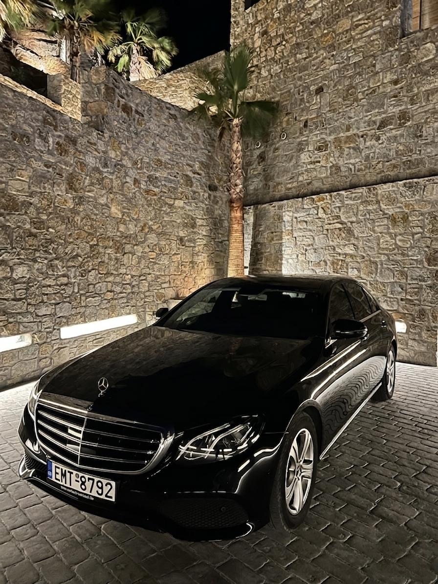Black Mercedes E-Class waiting at night by a lit stone wall on Mykonos