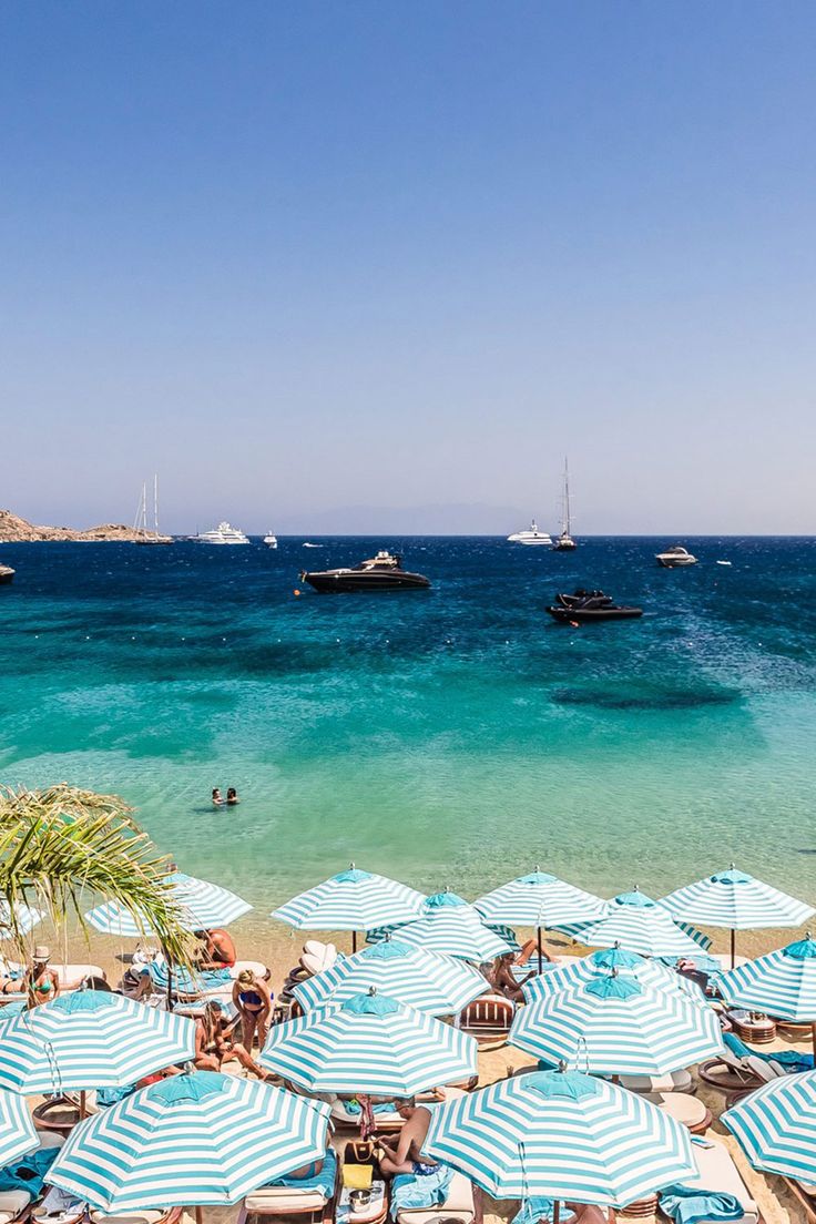 Striped umbrellas of a Mykonos beach club with yachts on the turquoise water